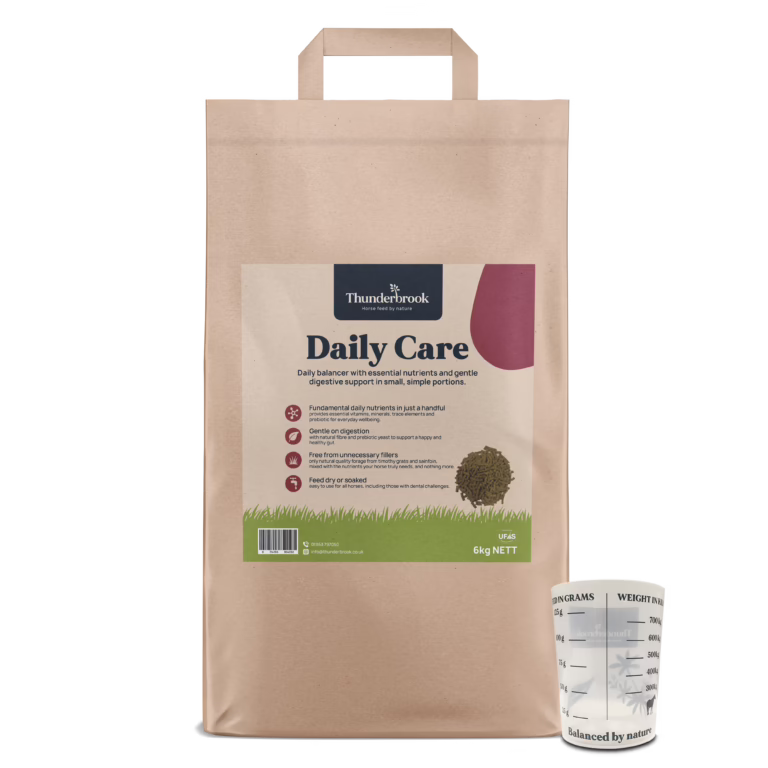 Front view of a brown paper bag labeled Thunderbrook Daily Care horse feed, with a white measuring cup beside it on the right.